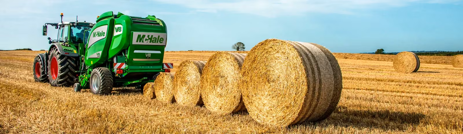 McHale V8 round baler with a row of finished bales in a stubble field