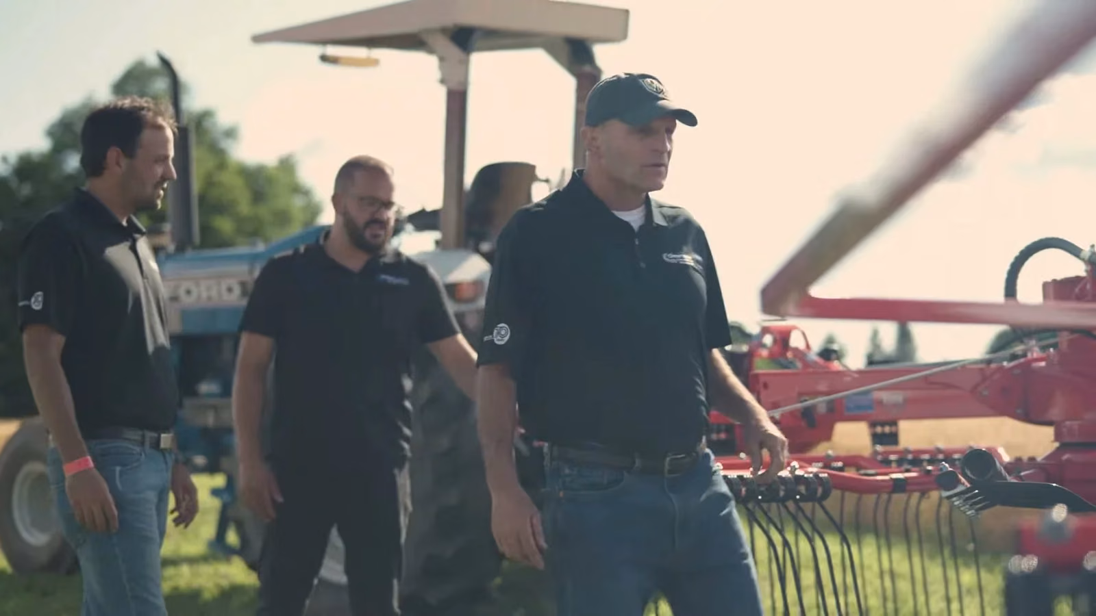 Three of the sales team beside a rake and tractor